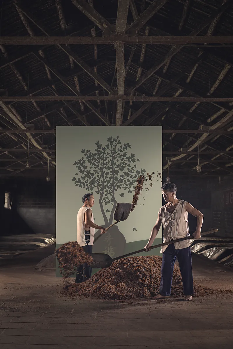 Two distillers turning a pile of grain; the painted tree behind them is in full leaf