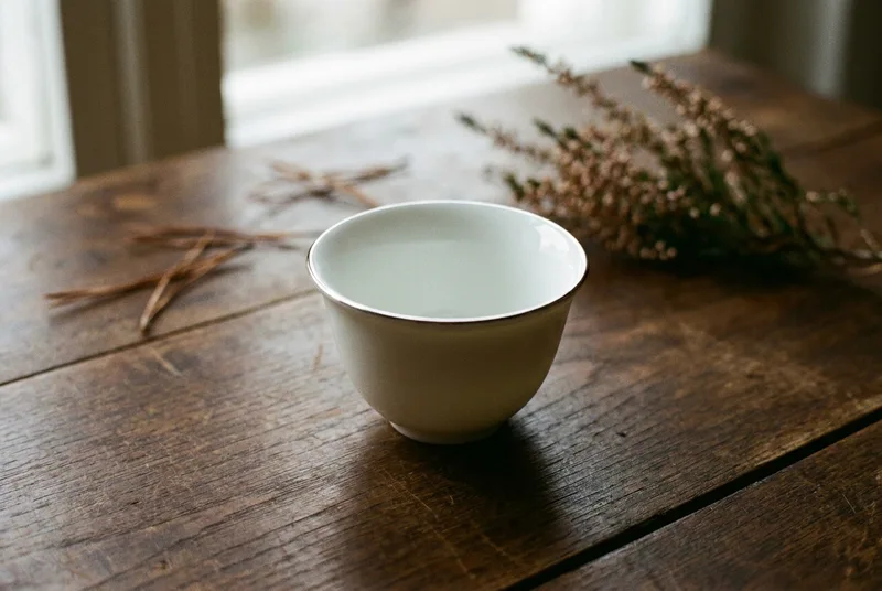 A small white porcelain tasting cup on a wooden table