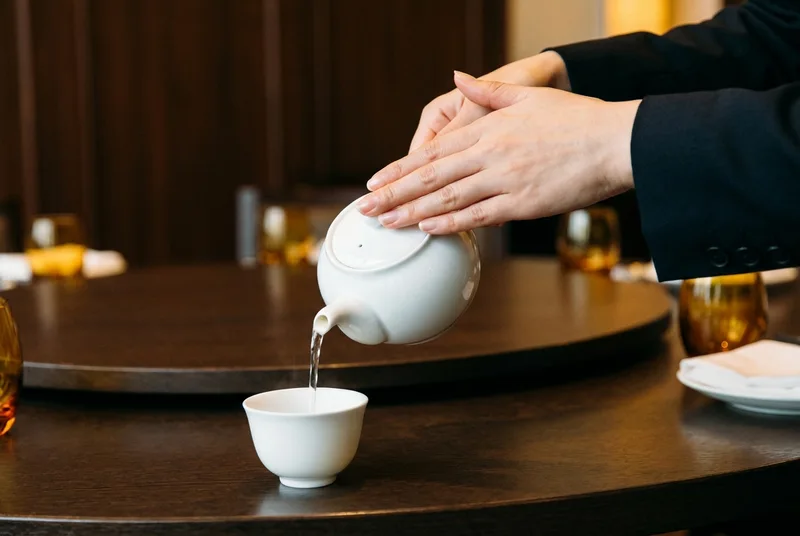 现代中式宴席上双手恭敬地将酒斟入瓷杯的特写