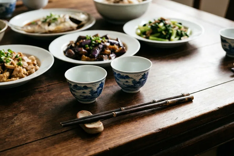 放在木桌上的两个小陶瓷酒杯与几道家常菜
