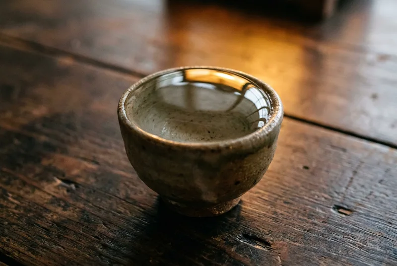 微距镜头下的一个小陶瓷品茗杯，杯中盛满了清澈的液体，表面张力让液体在杯沿形成完美的微凸弧面。