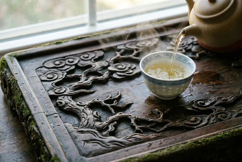 深色木质茶盘上的精美瓷茶杯，正被注入清澈的绿茶