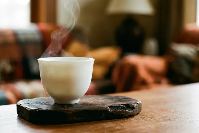 A delicate white porcelain wine cup on a dark wooden table, with a faint wisp of steam rising